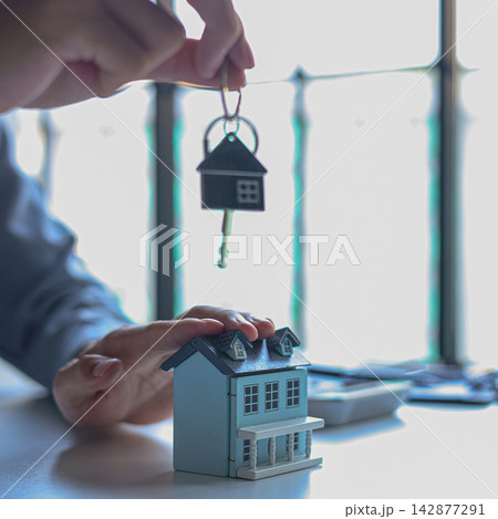 Hand holding key with house-shaped keychain. Concept for buying, selling, renting or leasing a new home. Hand holding key with house-shaped keychain. Concept for buying, selling, renting or leasing a new home. 142877291