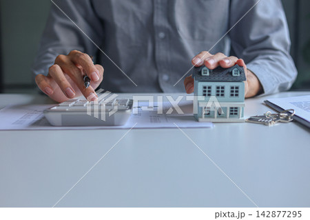 A person using calculator to determine costs of housing, such as mortgage payment, down payment or closing fees associated with property purchase. A person using calculator to determine costs of housing, such as mortgage payment, down payment or closing fees associated with property purchase. 142877295