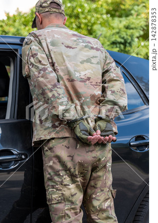 Detained man in military camouflage stands handcuffed beside a vehicle after a failed covert intelligence operation. Detained man in military camouflage stands handcuffed beside a vehicle after a failed covert intelligence operation. 142878353