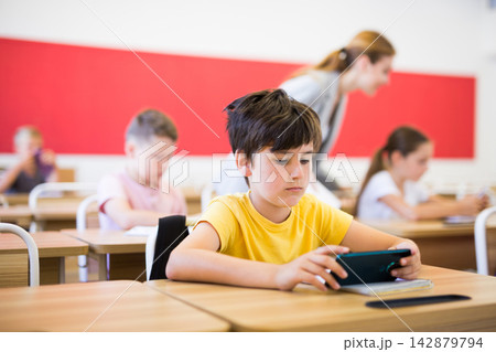 Focused tween schoolboy using mobile phone at lesson in class Focused tween schoolboy using mobile phone at lesson in class 142879794