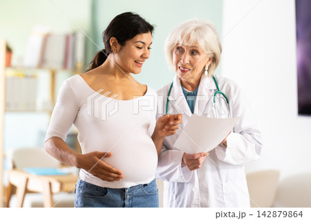 Friendly elderly doctor explaining good diagnostic results to happy pregnant 142879864