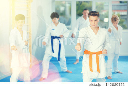 Group of focused teenages in kimonos practicing punches as part of kata 142880121