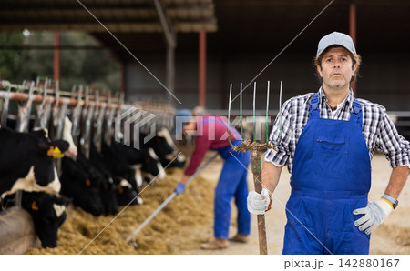 Farmer man stands with rake at cow farm 142880167