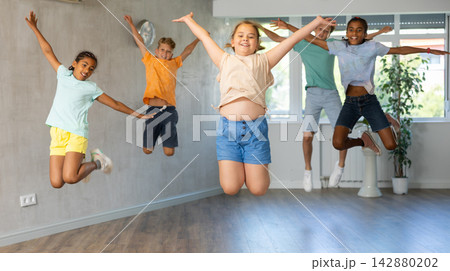 Female child engaged shake leg in fitness hall with friend, group of youthful people jumped into air 142880202
