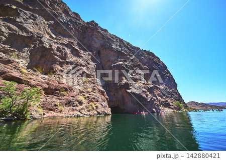 Kayakers on Colorado River Beside Rugged Cliffs and Clear Blue Sky in Arizona 142880421