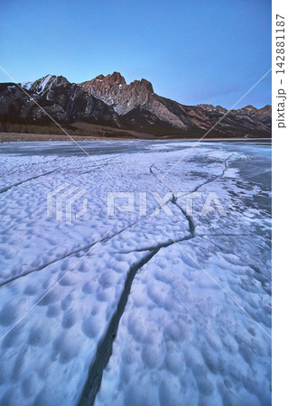 Frozen Lake Cracks and Rocky Mountains in Winter at Sunrise Alberta Canada 142881187