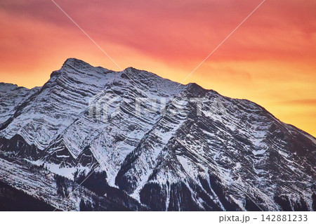 Snow Covered Rocky Mountain Peak with Vibrant Winter Sunset Sky 142881233