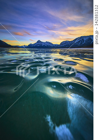 Frozen Lake Ice Patterns at Sunset with Dramatic Mountain Skyline Winter Landscape Frozen Lake Ice Patterns at Sunset with Dramatic Mountain Skyline Winter Landscape 142881312