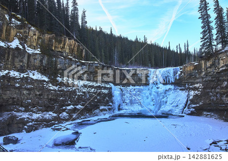 Frozen Waterfall and Rocky Cliffs with Snow and Forest in Winter Landscape Frozen Waterfall and Rocky Cliffs with Snow and Forest in Winter Landscape 142881625