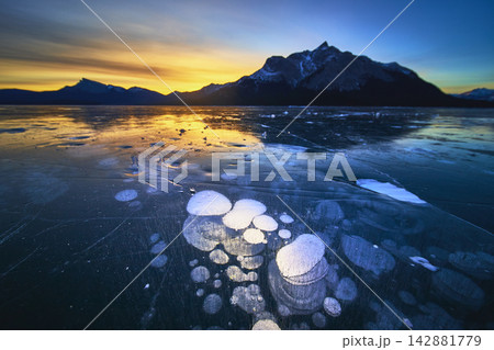 Frozen Methane Bubbles Under Clear Ice at Sunrise with Mountain Silhouettes Frozen Methane Bubbles Under Clear Ice at Sunrise with Mountain Silhouettes 142881779