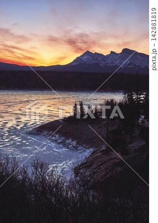 Winter Frozen Lake Sunset With Snowy Mountains And Pine Trees Winter Frozen Lake Sunset With Snowy Mountains And Pine Trees 142881819