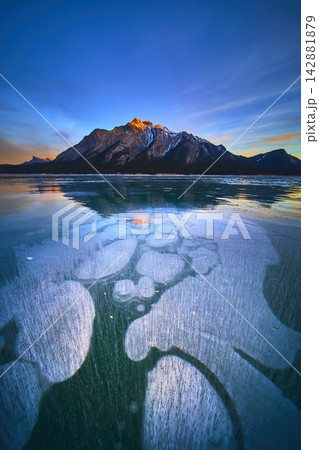Frozen Lake Methane Bubbles Blue Ice and Snow Capped Mountain at Winter Sunset 142881879