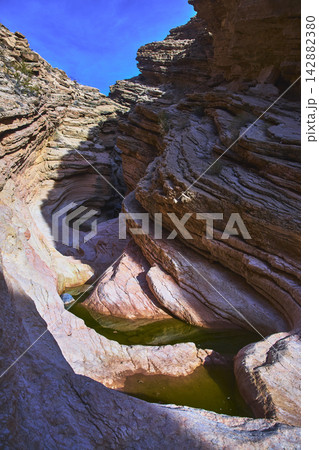 Desert Slot Canyon with Layered Rock Formations and Natural Water Pools Under Blue Sky Desert Slot Canyon with Layered Rock Formations and Natural Water Pools Under Blue Sky 142882380