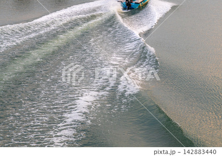 A motorboat moves across a calm lake, sweeping a curved wake of white foam and ripples. A motorboat moves across a calm lake, sweeping a curved wake of white foam and ripples. 142883440
