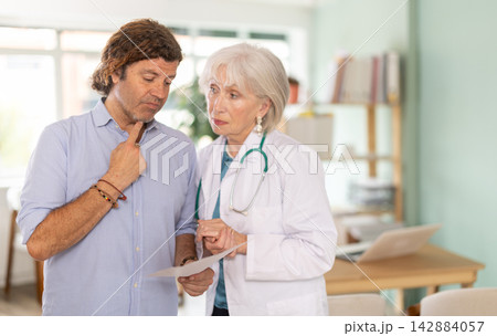 Elderly doctor discussing medical tests with sad man in medical office Elderly doctor discussing medical tests with sad man in medical office 142884057