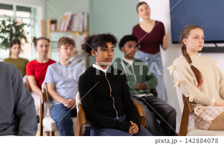Teenage students listening to lecture while teacher stands in background Teenage students listening to lecture while teacher stands in background 142884078