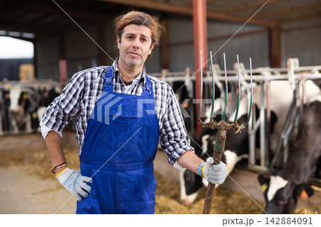 Farmer man stands with rake at cow farm Farmer man stands with rake at cow farm 142884091