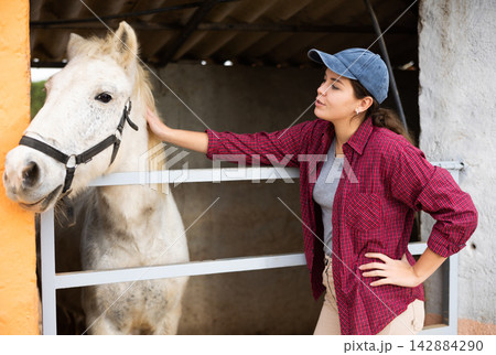 Female farmer standing near enclosure outdoors, talking to favorite horse Female farmer standing near enclosure outdoors, talking to favorite horse 142884290