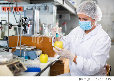 Female geneticist working in laboratory, injecting additives into apple during experiments with genetically modified apple 142884349