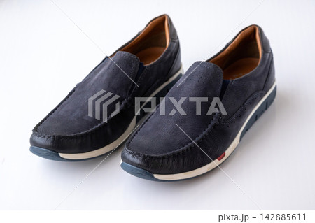 Pair of stylish navy blue leather slip-on loafers placed on white background. Modern casual footwear for male fashion, comfortable walking, and daily wear. Pair of stylish navy blue leather slip-on loafers placed on white background. Modern casual footwear for male fashion, comfortable walking, and daily wear. 142885611