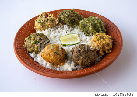 Authentic Bangladeshi steamed rice platter surrounded by traditional spicy mashed dishes including aloo, begun, chepa shutki, dim, and borboti bhorta with a lemon slice for lunch. 142885638