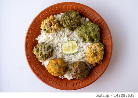 Traditional Bengali meal platter with steamed rice, served with assorted mashed bhorta including aloo, eggplant, dry fish, egg, and long beans, topped with fresh lemon slice, top view. 142885639