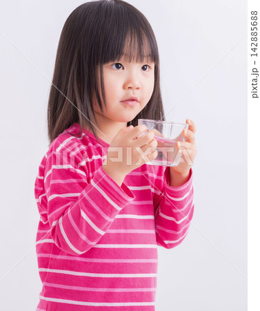 Cute little girl holding a glass and drinking fresh water against a white background. 142885688