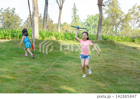 Energetic Asian girl running on a grassy slope and throwing a blue toy airplane into the air, aspiring to fly and childhood dream concept. Energetic Asian girl running on a grassy slope and throwing a blue toy airplane into the air, aspiring to fly and childhood dream concept. 142885847