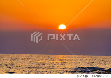 薄い雲の帯に沈む鮮やかなオレンジ色の海の夕日 142886288