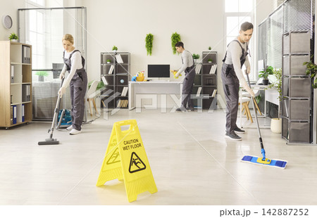 Cleaning crew mopping and vacuuming modern office with caution wet floor sign Cleaning crew mopping and vacuuming modern office with caution wet floor sign 142887252