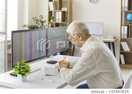 Senior accountant analyzing spreadsheet data on dual monitors in modern office Senior accountant analyzing spreadsheet data on dual monitors in modern office 142887624
