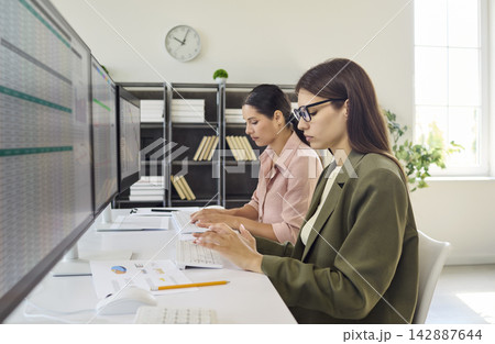 Women analysts working at computers, monitoring data and reports in office Women analysts working at computers, monitoring data and reports in office 142887644