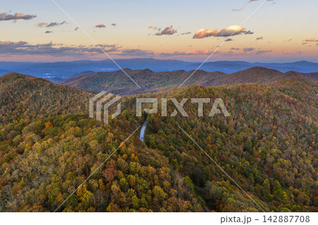 Road trip in evening fall season through dense forest. Car driving on a winding road under colorful autumn canopy. 142887708