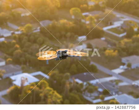 Camera drone in flight above suburban residential area, documenting urban planning, real estate layout and peaceful community lifestyle from elevated view. Camera drone in flight above suburban residential area, documenting urban planning, real estate layout and peaceful community lifestyle from elevated view. 142887756