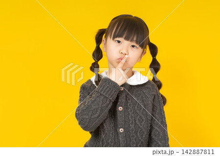 Cute little girl holding a finger to her lips for a silence gesture on a yellow background. Cute little girl holding a finger to her lips for a silence gesture on a yellow background. 142887811