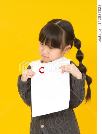 Little schoolgirl looking at her test paper with a bad grade C and feeling sad. Little schoolgirl looking at her test paper with a bad grade C and feeling sad. 142887828