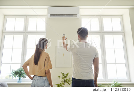 Couple using remote control to turn on air conditioner on wall of room at home Couple using remote control to turn on air conditioner on wall of room at home 142888019
