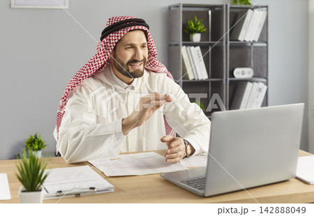 Videocall, virtual meeting and conversation of happy Arab businessman sitting at laptop in office Videocall, virtual meeting and conversation of happy Arab businessman sitting at laptop in office 142888049