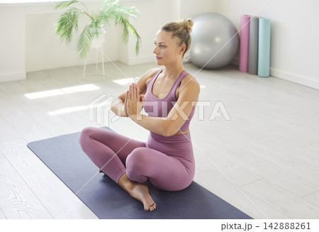 Woman practicing seated namaste yoga pose on mat in bright minimalist studio Woman practicing seated namaste yoga pose on mat in bright minimalist studio 142888261