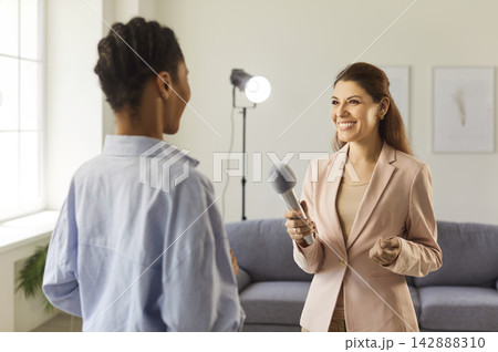Interviewer smiling and handing microphone to guest during studio recording Interviewer smiling and handing microphone to guest during studio recording 142888310