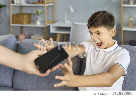 Angry boy screaming and grabbing smartphone during screen time conflict at home Angry boy screaming and grabbing smartphone during screen time conflict at home 142889090