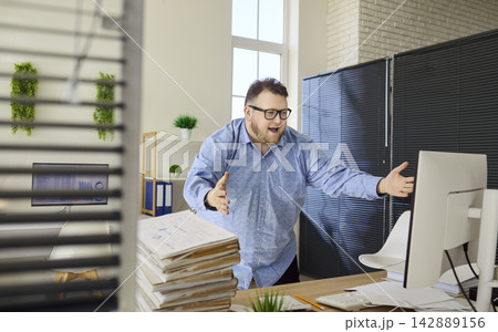 Stressed overweight office worker gesturing at computer with pile of paperwork Stressed overweight office worker gesturing at computer with pile of paperwork 142889156