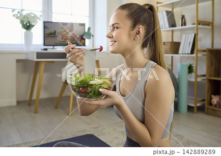 Fit woman eating salad at home after workout, healthy wellness lifestyle indoors 142889289