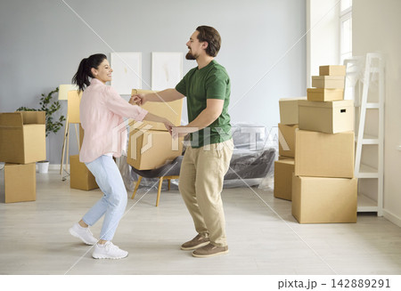 Happy couple dancing with moving boxes in new home, celebrating relocation teamwork Happy couple dancing with moving boxes in new home, celebrating relocation teamwork 142889291