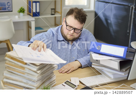 Accountant reviewing financial documents at desk during focused office paperwork Accountant reviewing financial documents at desk during focused office paperwork 142889507