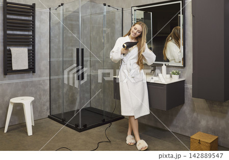Happy smiling young girl drying hair using hairdryer in modern bathroom interior Happy smiling young girl drying hair using hairdryer in modern bathroom interior 142889547