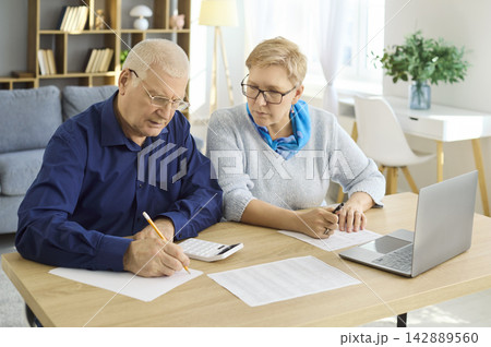 Senior couple reviewing bills signing documents with calculator and laptop Senior couple reviewing bills signing documents with calculator and laptop 142889560