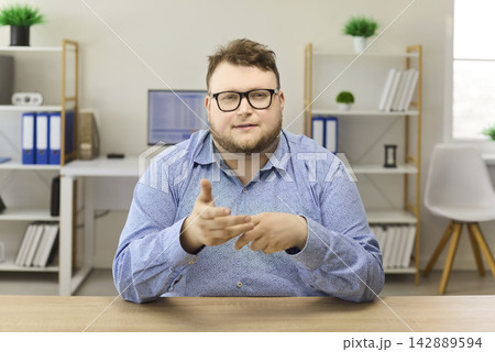 Confident businessman explains on video call in modern office during remote meeting Confident businessman explains on video call in modern office during remote meeting 142889594
