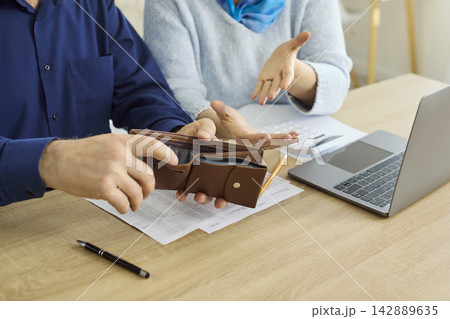 Senior couple checking empty wallet while budgeting and paying bills at home Senior couple checking empty wallet while budgeting and paying bills at home 142889635
