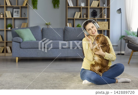 Happy woman in headphones hugging cocker spaniel at home on cozy living room floor Happy woman in headphones hugging cocker spaniel at home on cozy living room floor 142889720